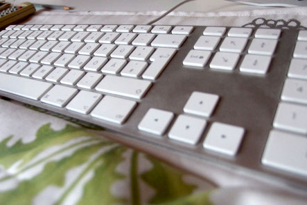 Man sieht eine Tastatur, davor eine selbstgenähte Handauflage aus Stoff, auf den Löwenzahnblätter gedruckt wurden.