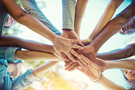 Eine Gruppe von Menschen unterschiedlicher Herkunft legt ihre Hände in der Mitte zusammen, darunter der Text „Zusammen sind wir stärker“.