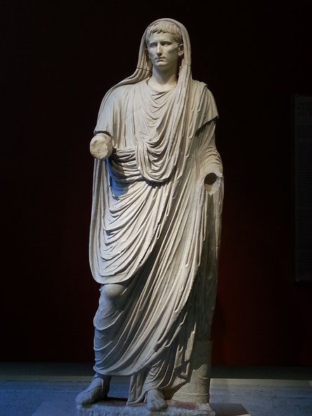 Full-body marble statue of a Roman figure draped in a toga with head covered, missing both forearms.