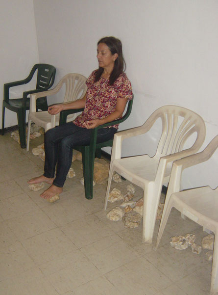 Un salón en donde hay sillas que tienen debajo piedras de cuarzo, hay una mujer meditando.