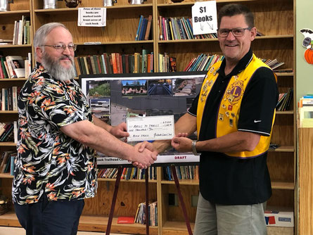 Neillsville Lions Club representative, Eric Backaus (right), presents a $1,000 donation to Neillsville Improvement Corporation Vice President, Dan Clough, for the Rails to Trails Project.