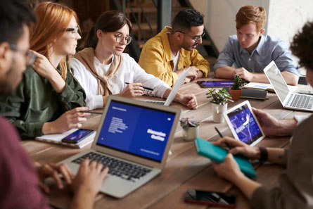 Junge Menschen sitzen im Rahmen einer Veranstaltung zur Berufsorientierung mit Laptops zusammen an einem großen Tisch
