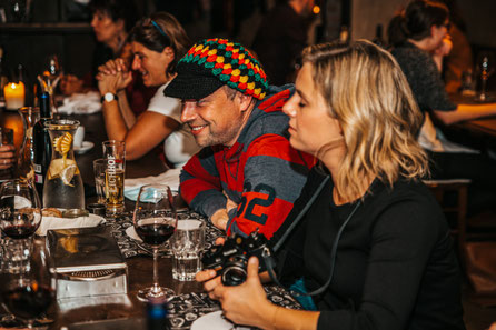 Die Gäste sitzen am Tisch. Sie trinken, essen und lachen während dem Krimi Dinner. Eine spannende Idee für ein Weihnachts- oder Firmenessen.