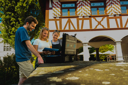 Eine gemischte Gruppe inspiziert auf ihrem Teamanlass in Luzern einen Rätselkoffer. Das Outdoor Escape Spiel bietet eine originelle Aktivität als Rahmenprogramm für den Teamevent.