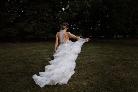eine Braut von hinten, das Tüllkleid weht in der Bewegung