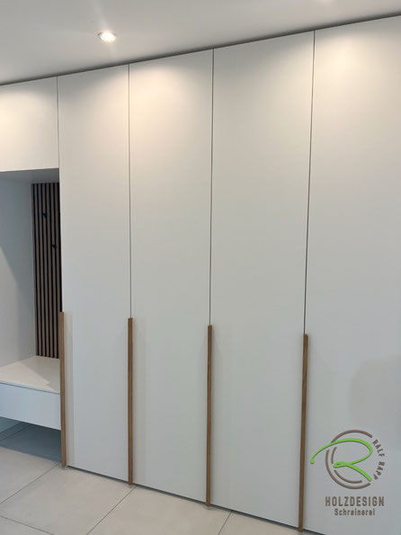 Maßgefertigter, deckenhoher Einbauschrank im Eingangsbereich vom Schreiner in der Nähe Stockach in der Bodenseeregion mit senkrechten Eiche Massivholz Griffleisten, weißen Fronten und offener Garderobennische mit Sitzbank u. Eiche Akustikelementen 