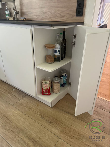 Schreinerküche für kleinen Raum mit praktischem Eckschrank der sich über Eck öffnen lässt und so für die maximalen Stauraumausnutzung sorgt und gedacht für geöffnete Getränkeflaschen und Vorräte die jederzeit griffbereit sein sollten