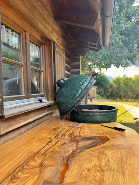 Massive Geisinger Esche mit bronzefarbigem Epoxidharz, eingefrästen Nussbaum-Holzfedern und Big Green Egg an einer Blockhütte bei Geisingen