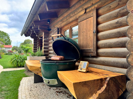 Outdoor-Küche mit Big Green Egg in massiver Geisinger Esche an einer Blockhütte nahe dem Wartenberg – naturgeschwungene Baumkante aus über hundert Jahre alter Esche mit Steak auf dem Keramikgrill
