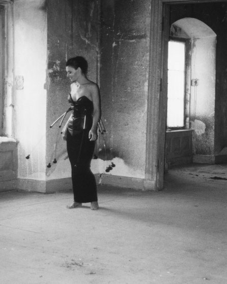 Ein schwarz-weißes Foto, in einer Schlossruine aufgenommen. Eine Frau steht in einem schwarzen kunstvollen Kleid vor dem Fenster.