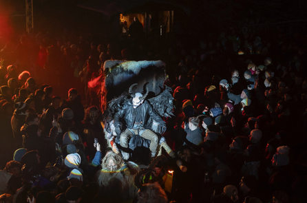 Teufelsfigur mit Hörnern und Flügeln wird von einer großen Menschenmenge umringt.