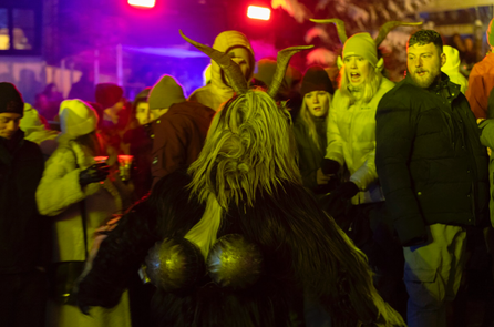 Krampusfigur mit Fell und Hörnern läuft durch eine Gruppe von Besucher:innen im bunten Bühnenlicht.