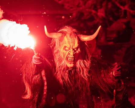 Krampusfigur in rotem Licht mit brennender Fackel.