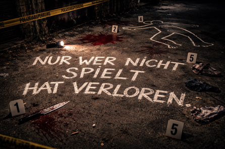 Wer nicht spielt hat verloren. Das Bild zeigt ein abgesperrter Tatort und die Umrisse einer Leiche sowie ein Messer und alte Kleidungsstücke. Was ist hier passiert? Löst die Rätsel als Team und überführt den Mörder, bevor die Zeit abgelaufen ist.