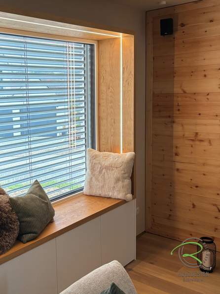 Fenstersitz mit umlaufenden Eichen Rahmen mit stimmungsvoller LED-Beleuchtung, Wohnzimmer mit maßgefertigtem Sitzfenster aus Eiche und weißem Unterschrank – Schreinerarbeit von Holzdesign Ralf Rapp, Radolfzell am Bodensee. Perfekt für modernes Wohnen 