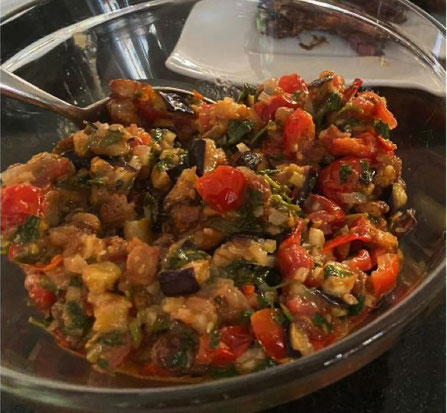 Glasschüssel mit Auberginensalat mit kleingeschnittenen Auberginenstückchen, Tomaten, Sellerie, Rosinen und Petersilie