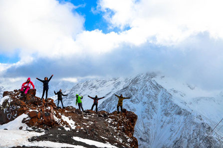 Bergsteigende strecken ihre Arme hoch und sind auf einem Berggipfel