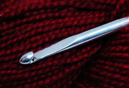 Sterling silver crochet hook threaded through a ball of red yarn.