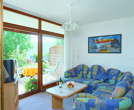 Das gemütliche Wohnzimmer im Wintergarten mit überdachter Südterrasse und direkten Zugang auf Liegewiese und Garten.