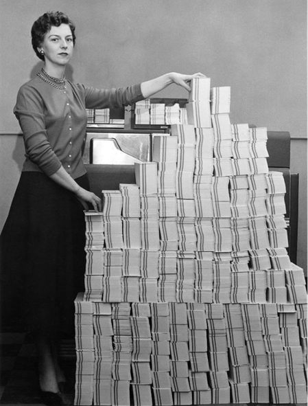 Una programmatrice con la pila di migliaia di schede perforate di un programma