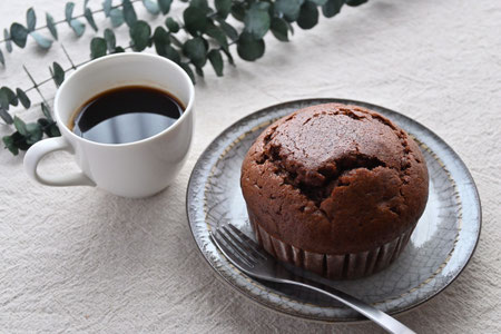 チョコレートマフィンのお皿とコーヒーの入ったマグカップ。ユーカリの小枝。