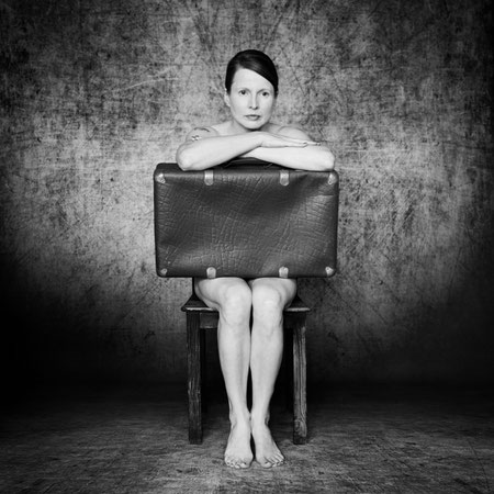 Manuela Deigert Mittelformat, künstlerisches Selbstportrait in schwarzweiß, mittig auf einem Stuhl sitzend mit einem Koffer auf dem Schoß