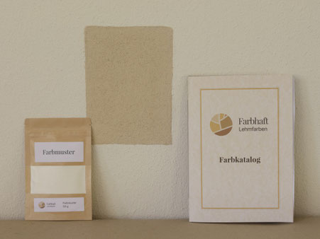 Farbmuster und Farbkatalog vor heller Lehmwand mit gestrichener Testfläche.