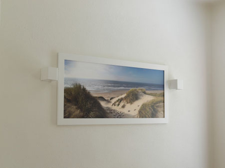 Schlafzimmerwand mit matter Lehmfarbe in Marmorweiß und gerahmtem Landschaftsbild.