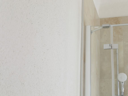Wand mit Lehmfarbe in Marmorweiß neben einer verglasten Dusche, außerhalb des direkten Spritzwasserbereichs.