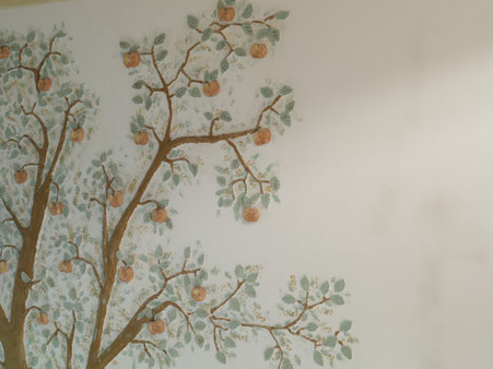 Handgemaltes Apfelbaum-Motiv mit Ästen, Blättern und Äpfeln auf einer hellen Wandfläche in Marmorweiß.