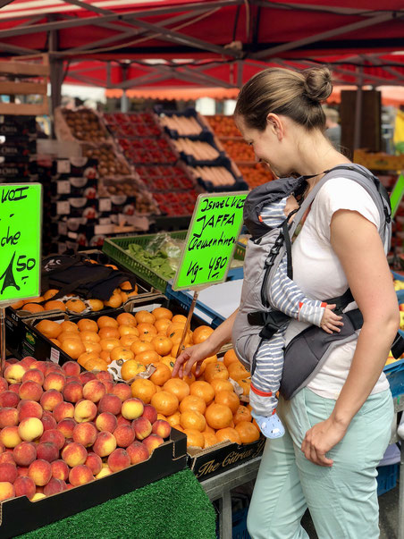 Mutter mit Baby auf Wochenmarkt am Obststand mit Mandarinen und Pfirsichen, frisches Obst