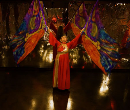 Woman dancing with flags with gold trumpets and multicolored field.