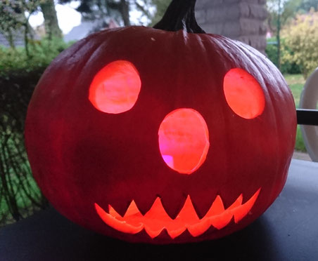 Selbst geschnitzter Halloween-Kürbis mit ovalen Augen, einer ovalen Nase und einem Mund voller spitzer Zähne, der von innen rötlich leuchtet