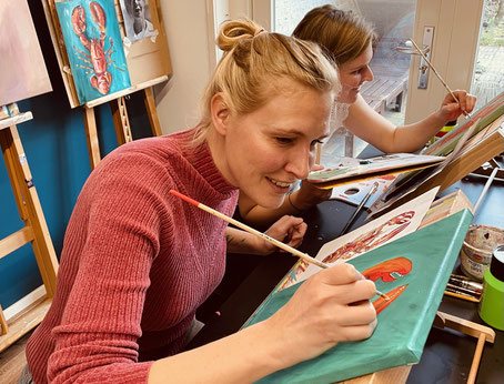 Deelnemers aan een Sip&Paint-workshop in het atelier van Daphne Schrijver in Breda, ontspannen aan het schilderen aan kleurrijke kreeft-schilderijen.