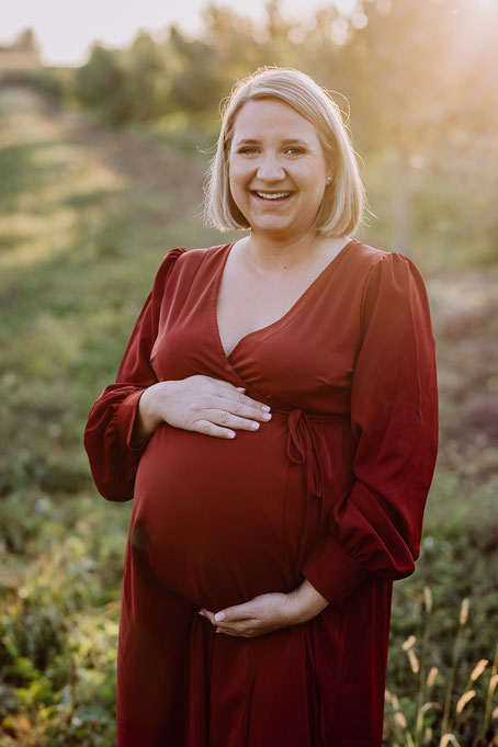 eine schwangere Frau in rotem Kleid steht auf einer Wiese