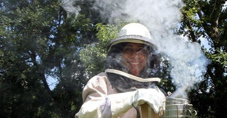 Jenny Castro demonstrates the screened helmet, long-sleeve gloves and other clothing that protect beekeepers, and the smoker used to calm bees while working in the beehive. ANDY JONES/STAFF