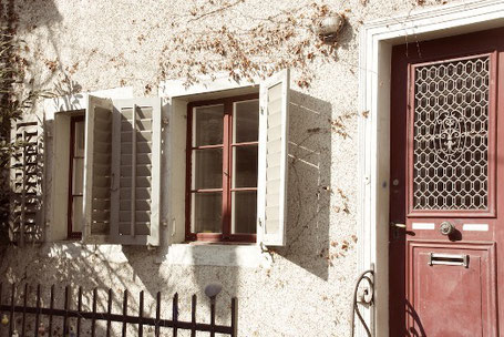 Zwei Fenster mit roten Rahmen, geöffneten Läden und einer roten Tür rechts