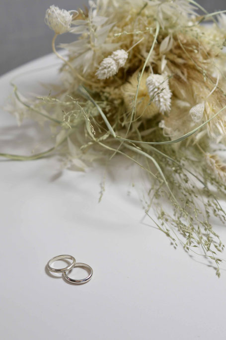 Deux alliances en or blanc sur une table avec un bouquet de mariées en fleurs séchées