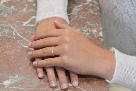 mains de femmes posées  sur une table en marbre brun portant un fin anneau en or jaune entièrement serti de diamants