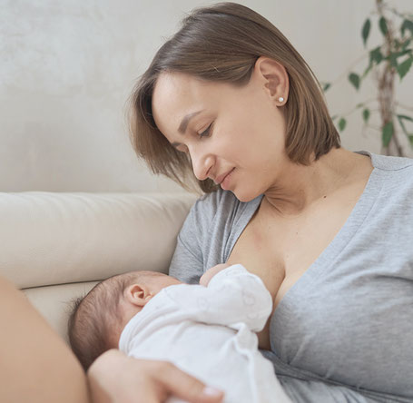 Eine Frau mit 30 Jahren hält ihr Baby in der Hand und lächelt. 