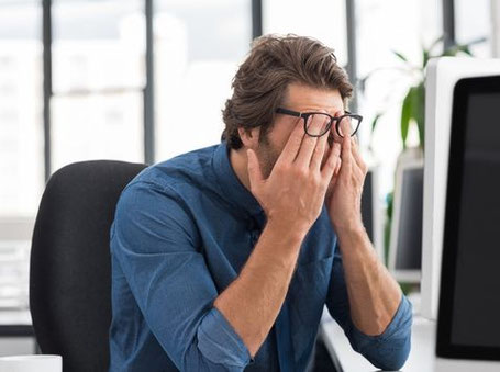 Ein Mann sitzt am Schreibtisch, die Hände vor dem Gesicht zusammengelegt. Er runzelt die Stirn.