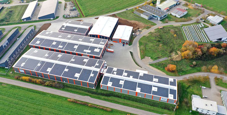 Sechs Lagerhallen-Neubauten sind von einer Drohne fotografiert: Auf vier Lagerhallen erkennt man deutlich Fotovoltaik-Anlagen.