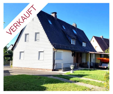 Ein Haus mit weißer Holzfassade, mit kleinen überdachten Terrasse und einem orangenen Schaukelsessel. Dieses Haus steht in Herzogenaurach und wird durch Kollmer IMMOBILIEN verkauft. Es ist ein Immobilienangebot.