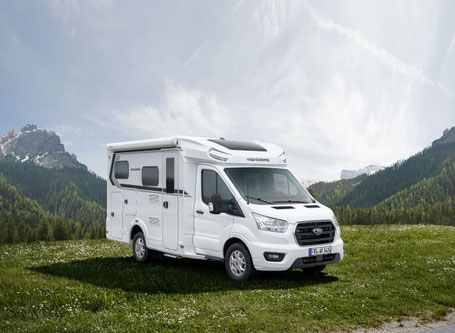 Kleines weißes Wohnmobil steht auf einer Wiese vor Berg 2025