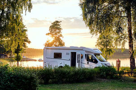 Weißes Teilintegriertes Wohnmobil an einem See in Abendstimmung