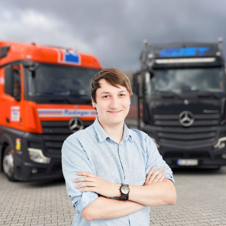 Herr Jonas Sauerland lächelt in die Kamera. Hinter ihm stehen 2 Lkw.