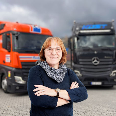 Frau Kerstin Tintrup lächelt in die Kamera. Hinter ihr stehen 2 Lkw.