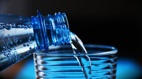 Foto einer Wasserflasche, aus der gerade Wasser in ein Glas gegossen wird.