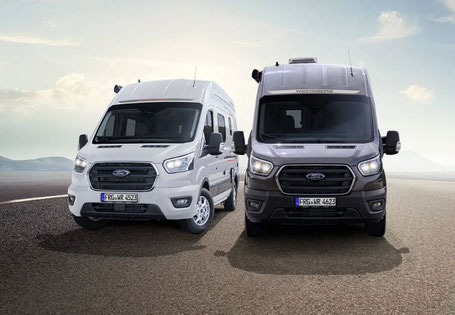 Zwei moderne Kastenwagen in weiß und Dunkelgrau nebeneinander auf Asphalt vor dramatischem Wolkenhimmel