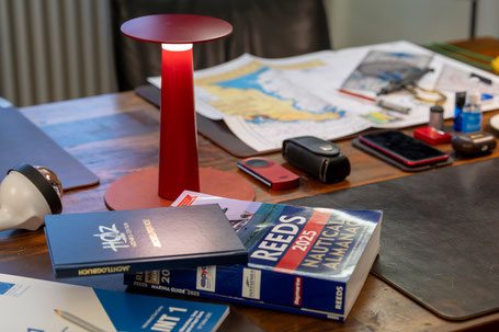 Schreibtisch mit nautischer Fachliteratur, Karten und Lampe – Symbol für Studium, Präzision und praxisnahe Navigation.